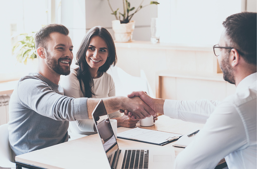 Cheerful young man and woman shaking hand to man sitting in front of him across the desk